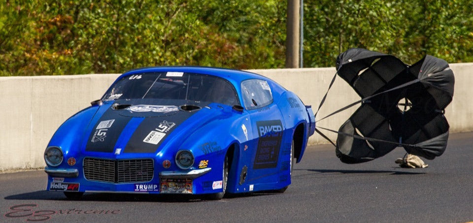 Blue race car with a parachute on a track, surrounded by various sponsor logos.