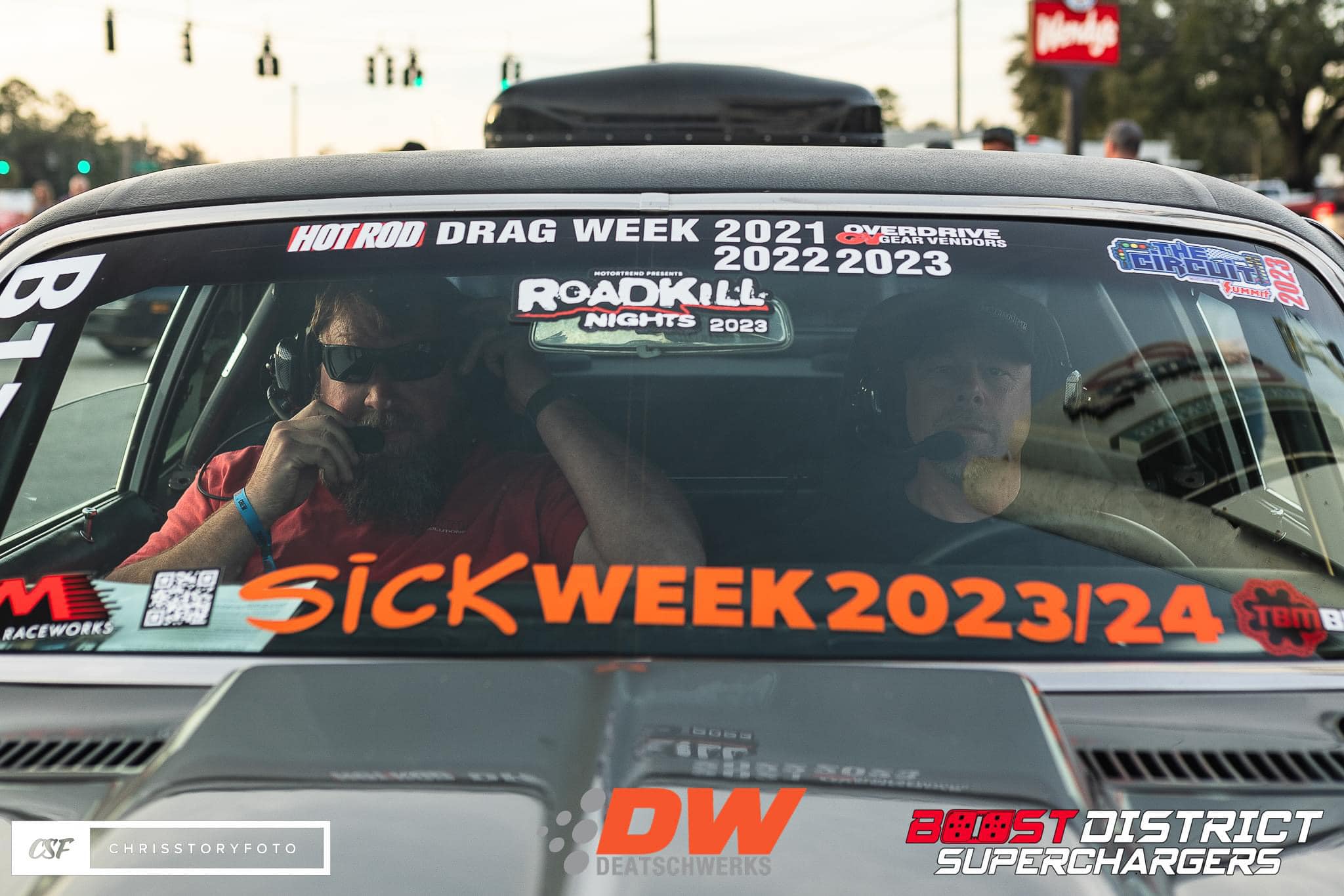 Car with various stickers on the windshield, including 'Sick Week 2023/24' and 'Drag Week 2021-2022-2023'.